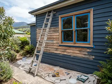 Weatherboards sanded and masked for painting, with drop sheets and a ladder
